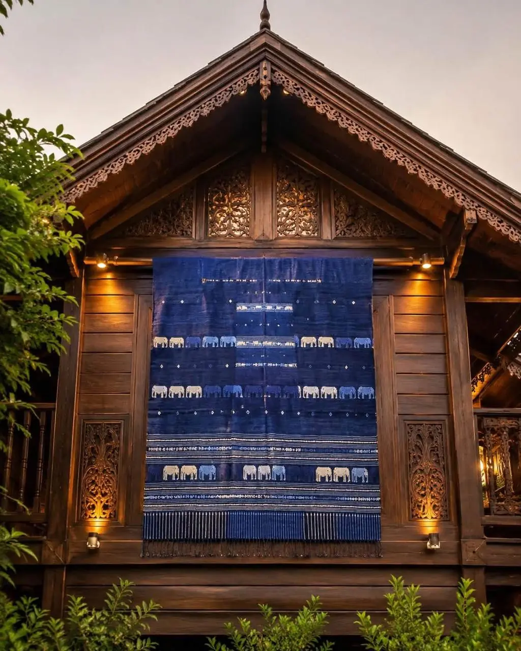 Indigoblaues Webtuch mit Reihen von Elefantenmotiven, aufgehängt an einem traditionellen Holzhaus